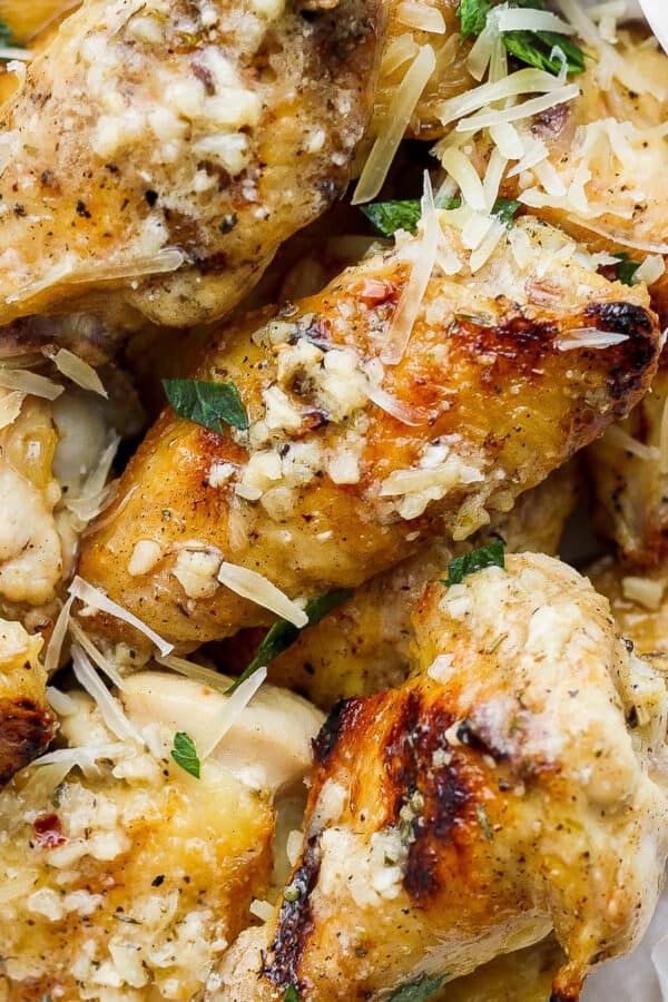 A bowl lined with parchment filled with garlic parmesan wings topped with extra shredded parmesan and fresh parsley.