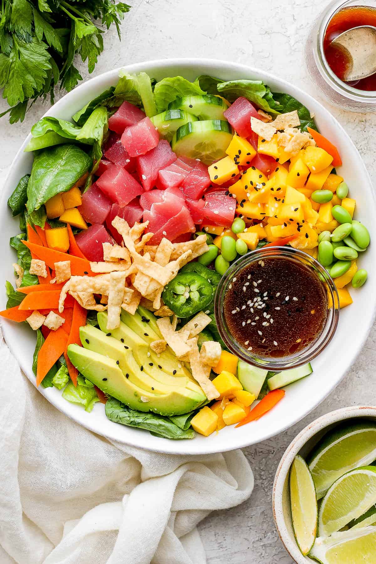 Bowl of poke salad with mango, avocado, carrots, edamame, jalapeno and a small bowl of sauce.