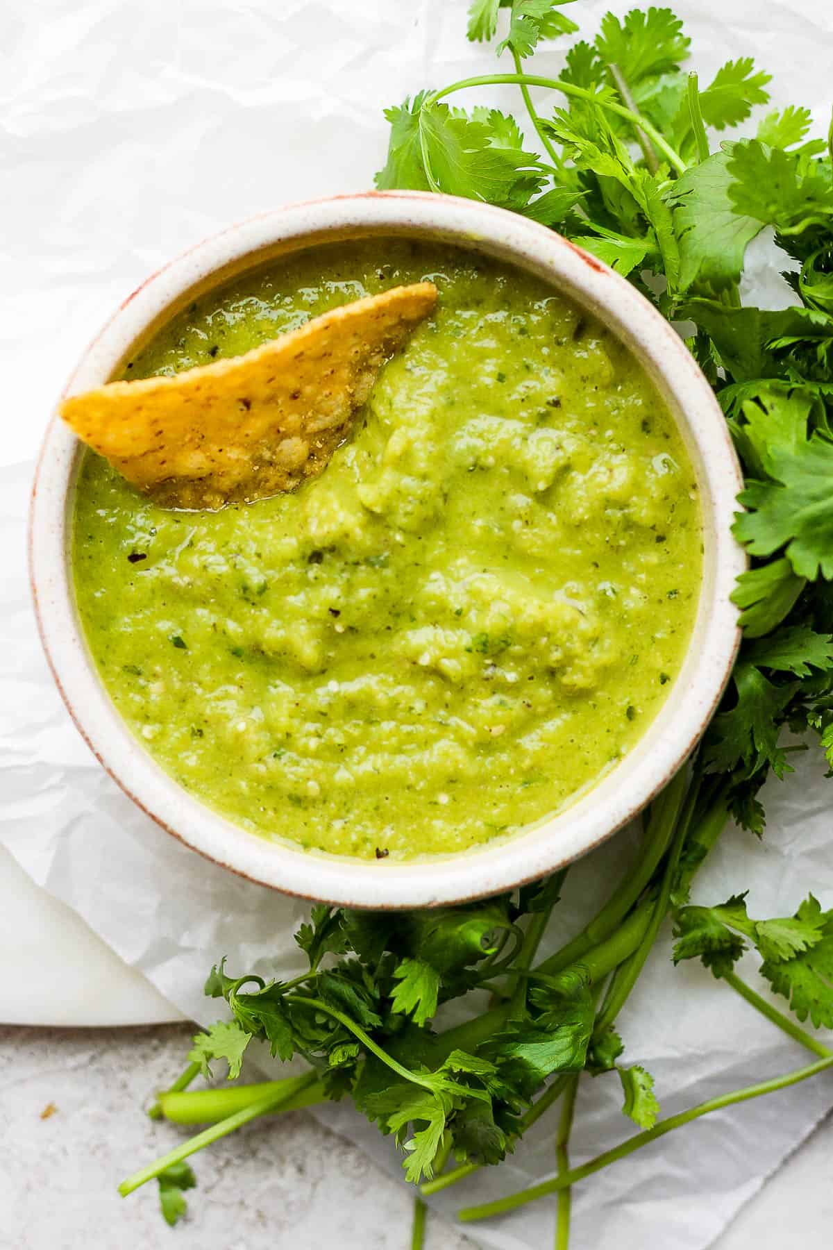 A small bowl of salsa verde with a tortilla chip in it.