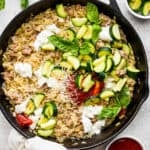 Top down shot of a cast iron skillet filled with a sausage zucchini skillet with cheesy orzo and topped with marinara and fresh basil.