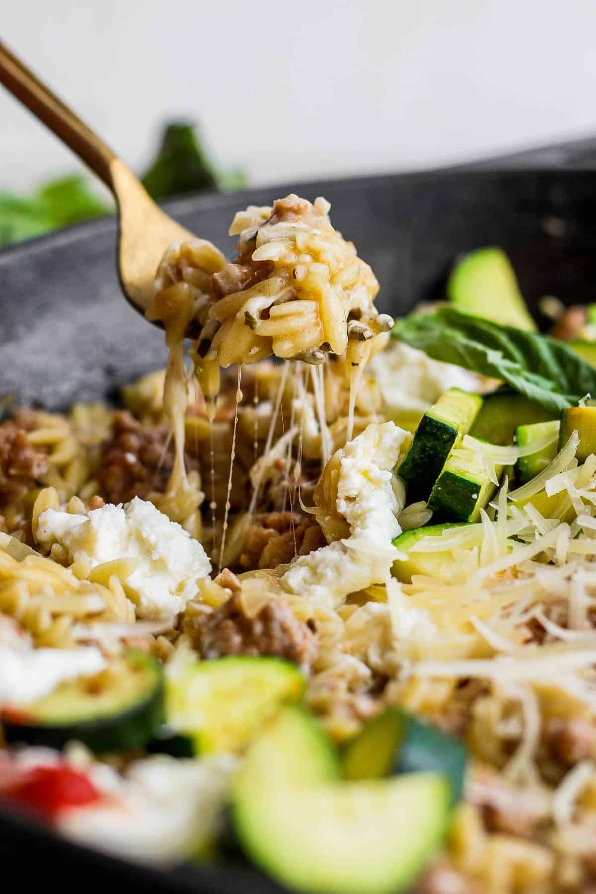 A fork scooping some of the sausage zucchini skillet out of the skillet.