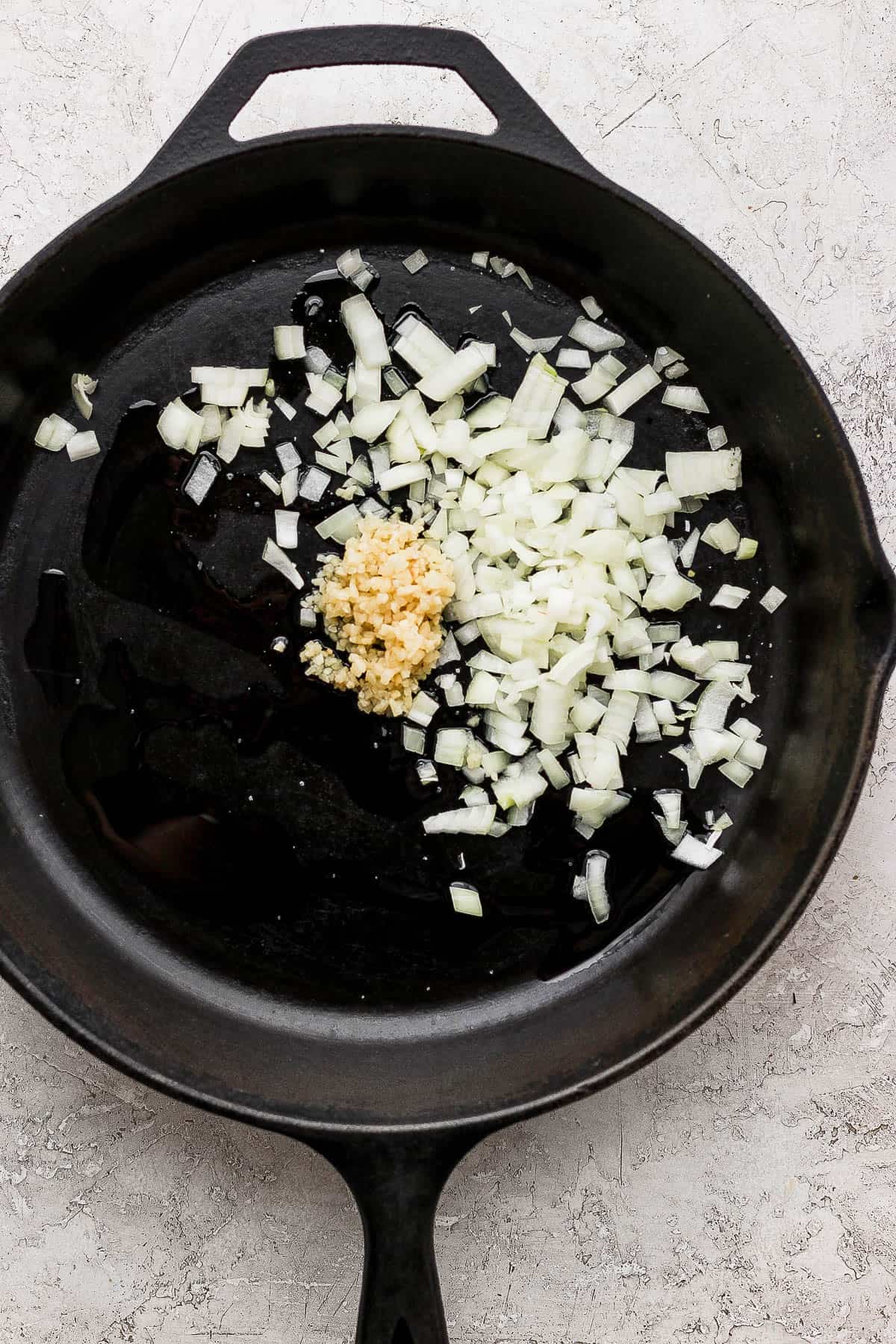 A cast iron skillet with onion and garlic sautéing in it.