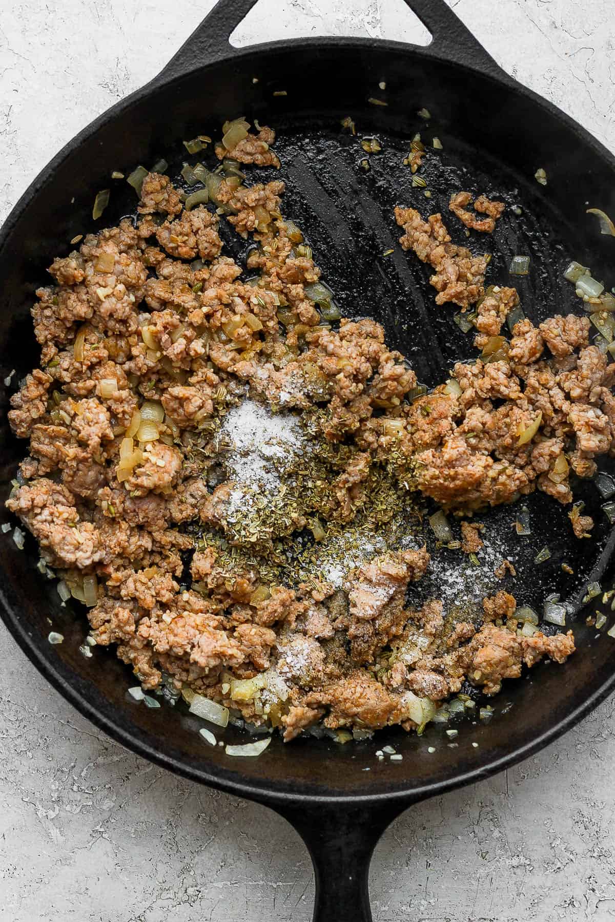 A skillet with browned Italian sausage and seasonings added.