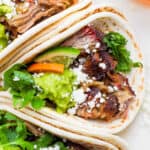 Top down shot of a smoked carnitas taco with cilantro, guacamole, lime wedge and cotija cheese crumbles.