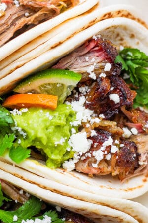 Top down shot of a smoked carnitas taco with cilantro, guacamole, lime wedge and cotija cheese crumbles.
