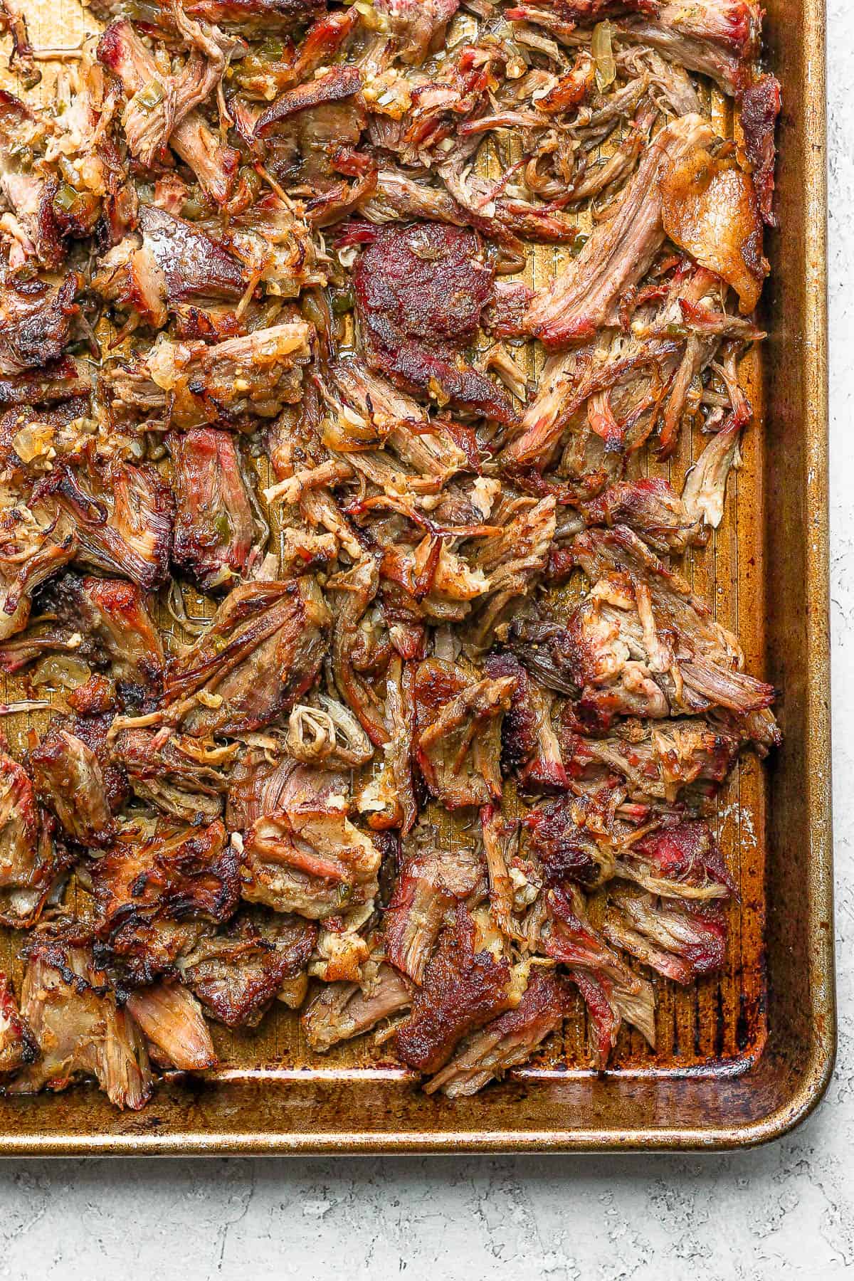 The smoked pork pulled apart and placed on a rimmed baking sheet with some braising liquid poured over the top.