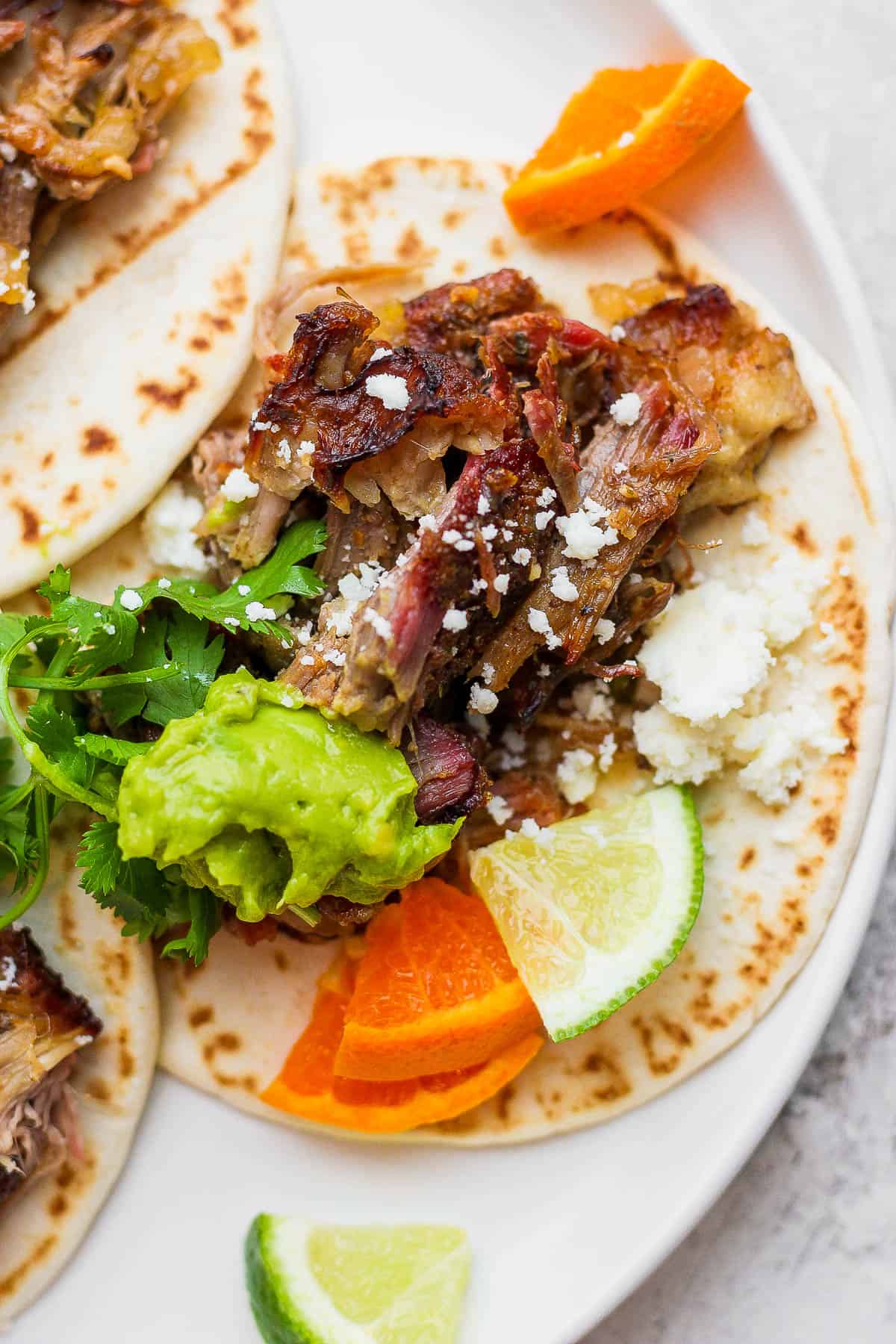 A smoked carnitas taco on a white plate with the toppings added.