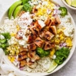 A bowl with rice, grilled chicken, mexican street corn, cilantro and limes.