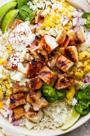 A bowl with rice, grilled chicken, mexican street corn, cilantro and limes.