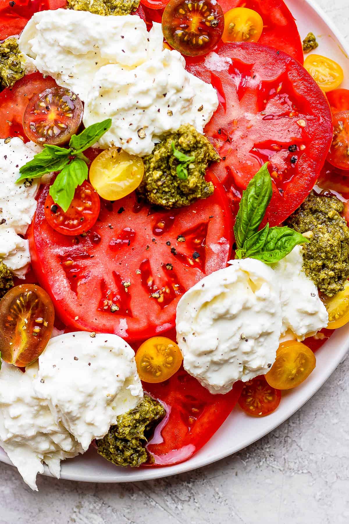 A fully assembled tomato burrata salad on a platter before the olive oil is added on top.