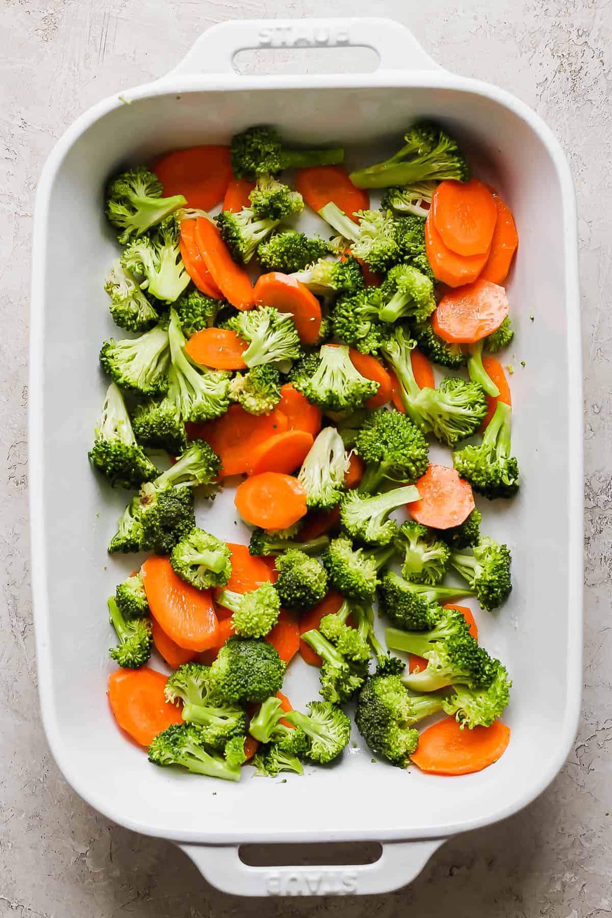 Broccoli florettes and sliced carrots in the bottom of a baking sheet.