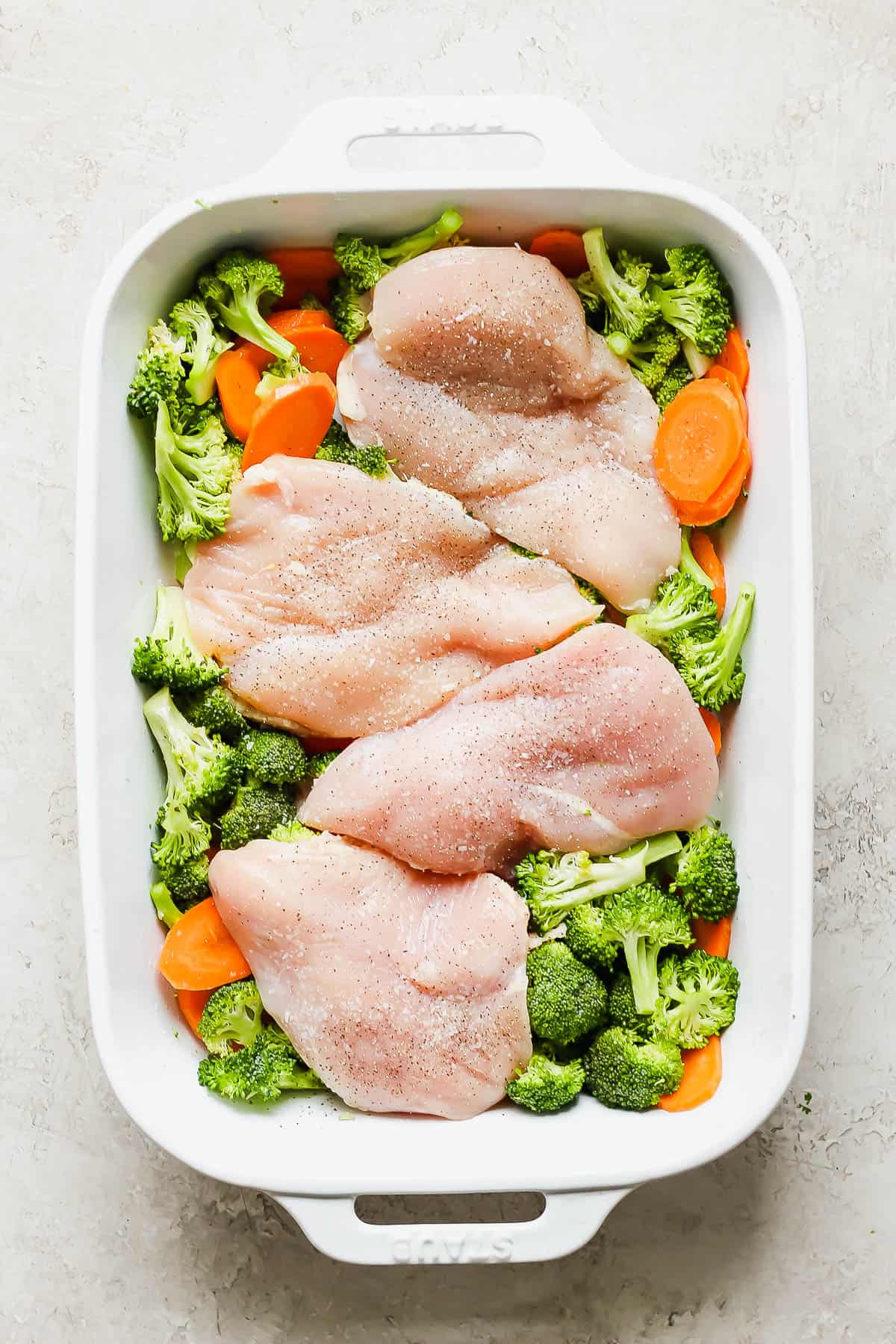 Seasoned chicken breasts on top of the veggies in the baking sheet.