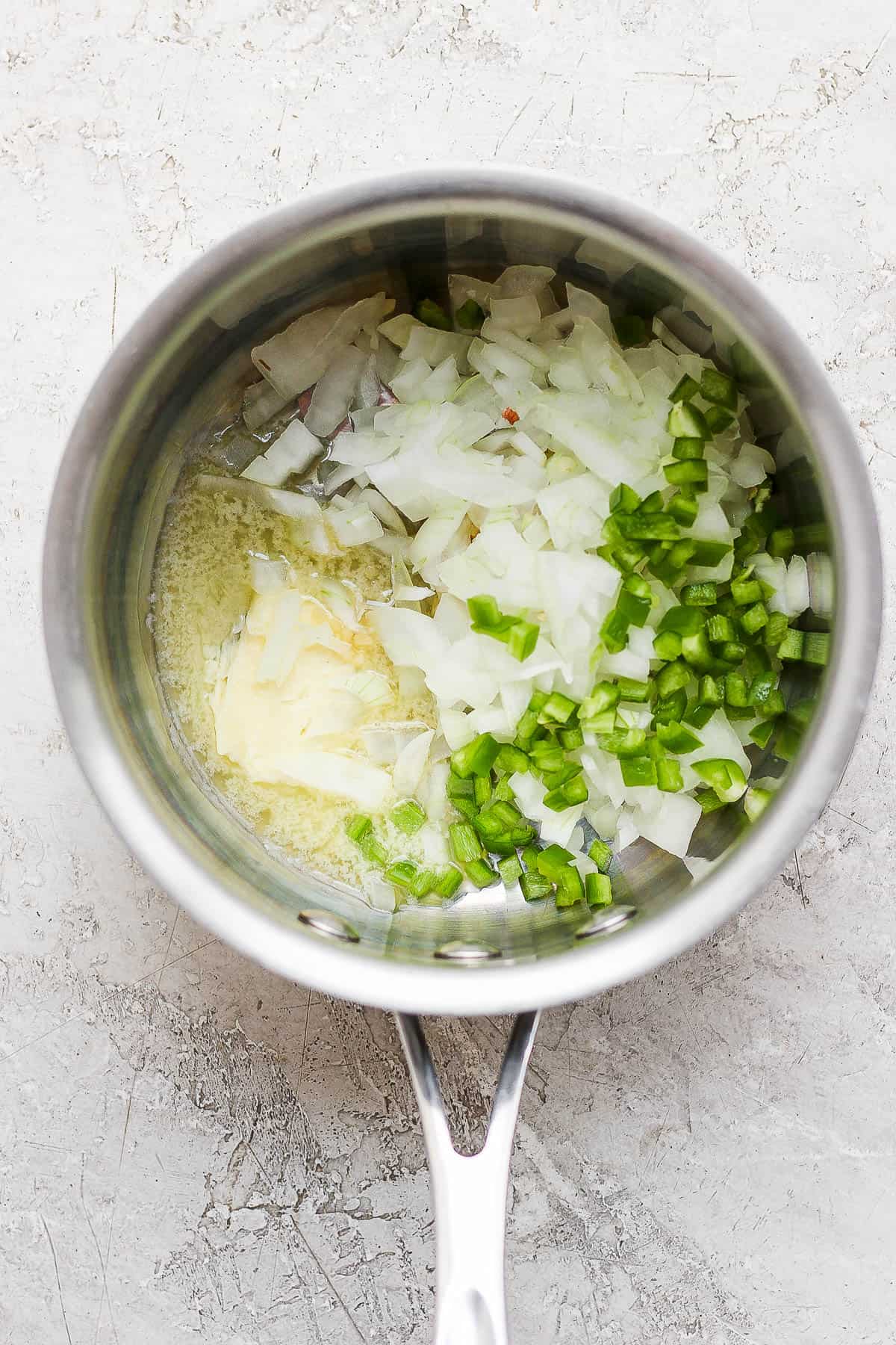 Butter melted in a saucepan with onion, garlic, and jalapeno added to the pot.