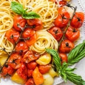 Top down shot of a plate of cherry tomato pasta with fresh basil leaves.