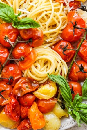 Top down shot of a plate of cherry tomato pasta with fresh basil leaves.