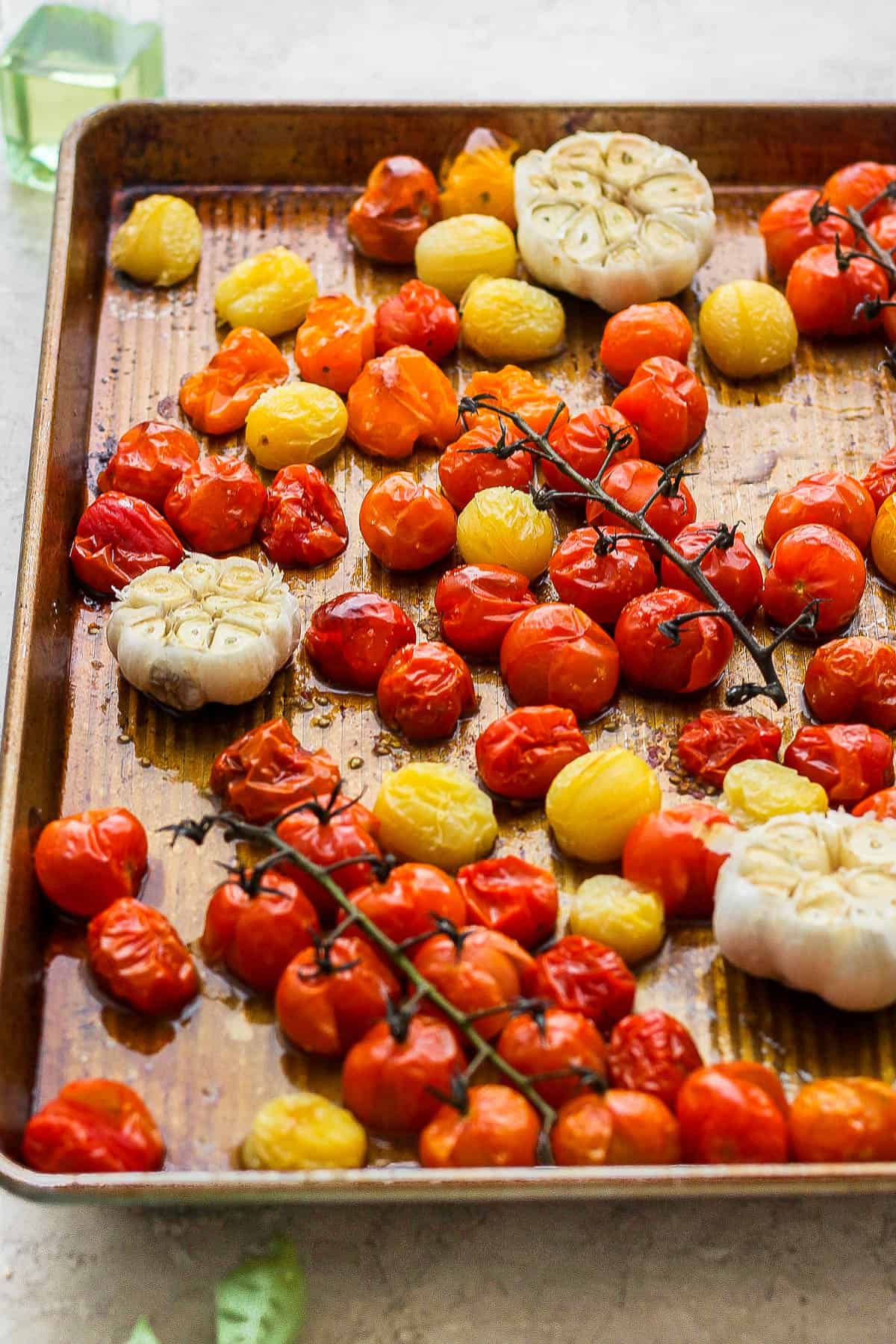 Roasted garlic cloves and cherry tomatoes on a baking sheet.