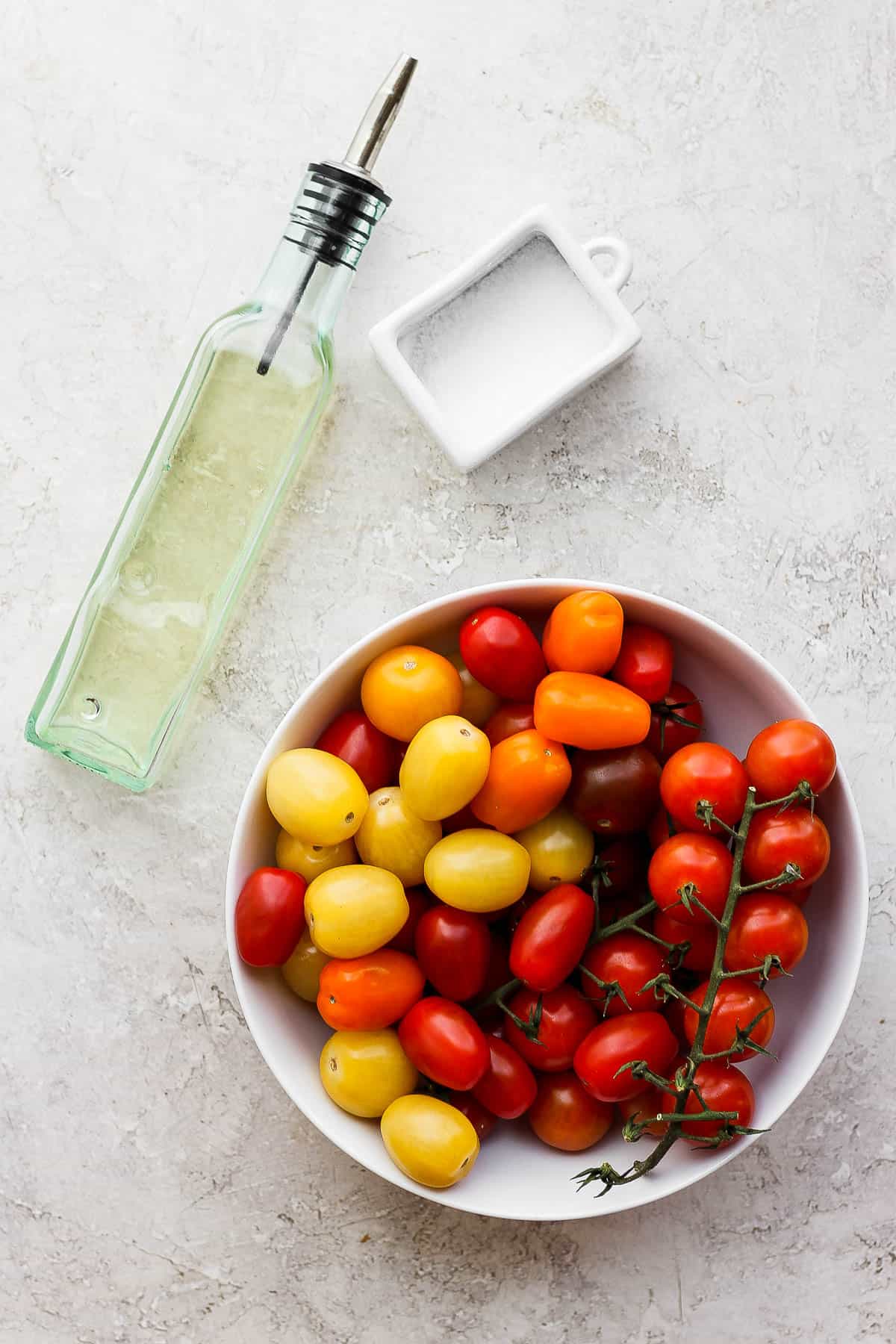 A bowl of cherry tomatoes, a container of salt, and a container of olive oil on a counter.