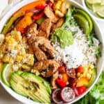 Top down shot of a chicken fajita bowl with rice, corn, avocado, tomatoes, veggies and chicken.