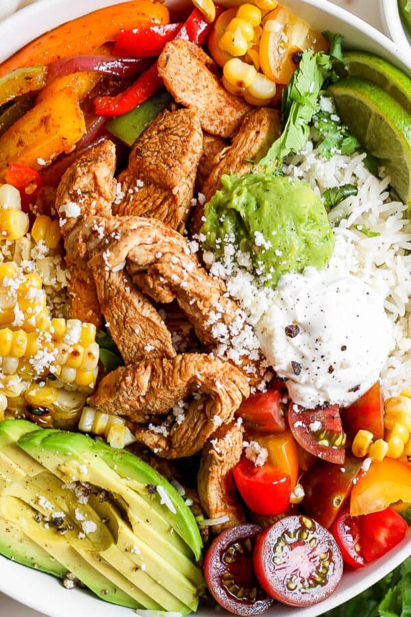 Top down shot of a chicken fajita bowl with rice, corn, avocado, tomatoes, veggies and chicken.