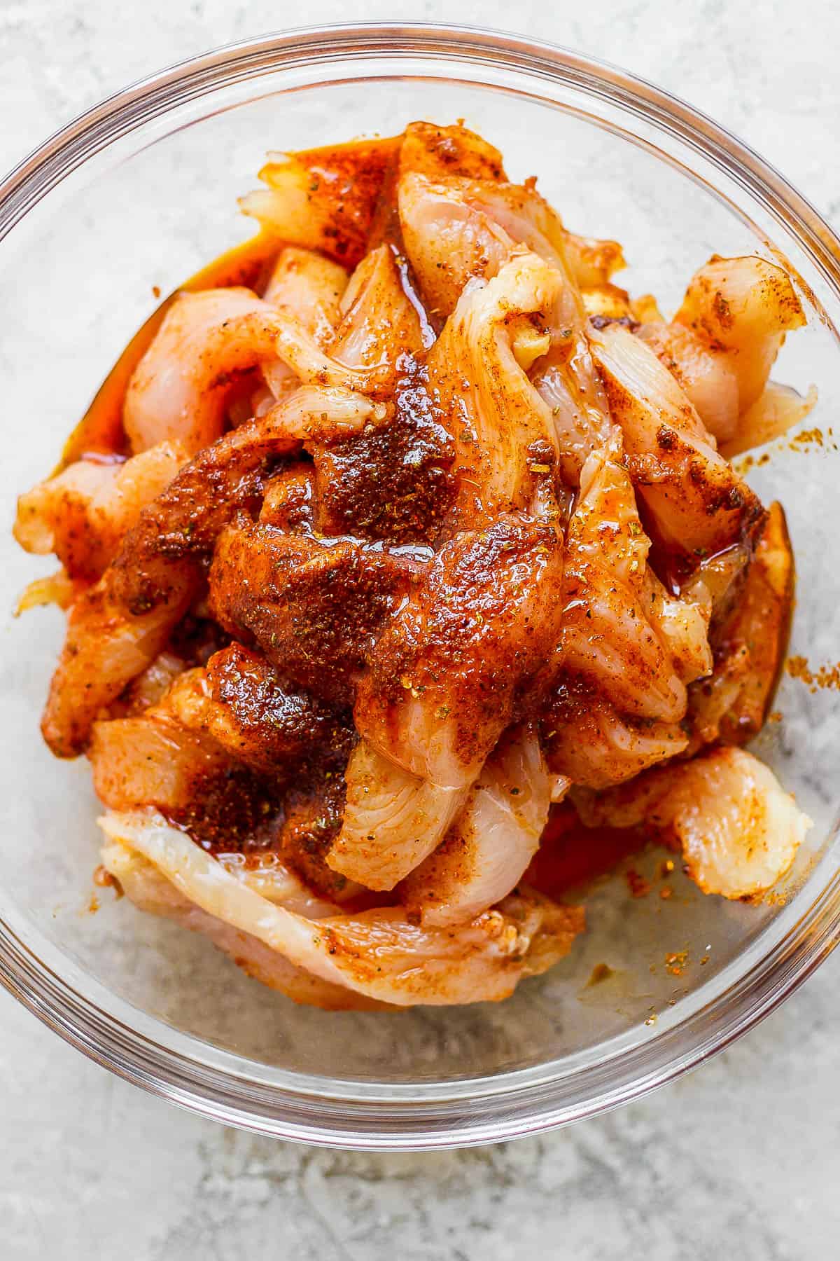 Chicken fajita marinade poured over chicken tenders in a large, glass bowl.