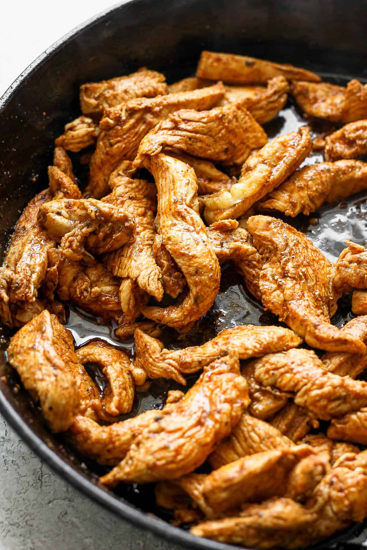Marinated chicken tenders cooking in a large cast iron skillet.