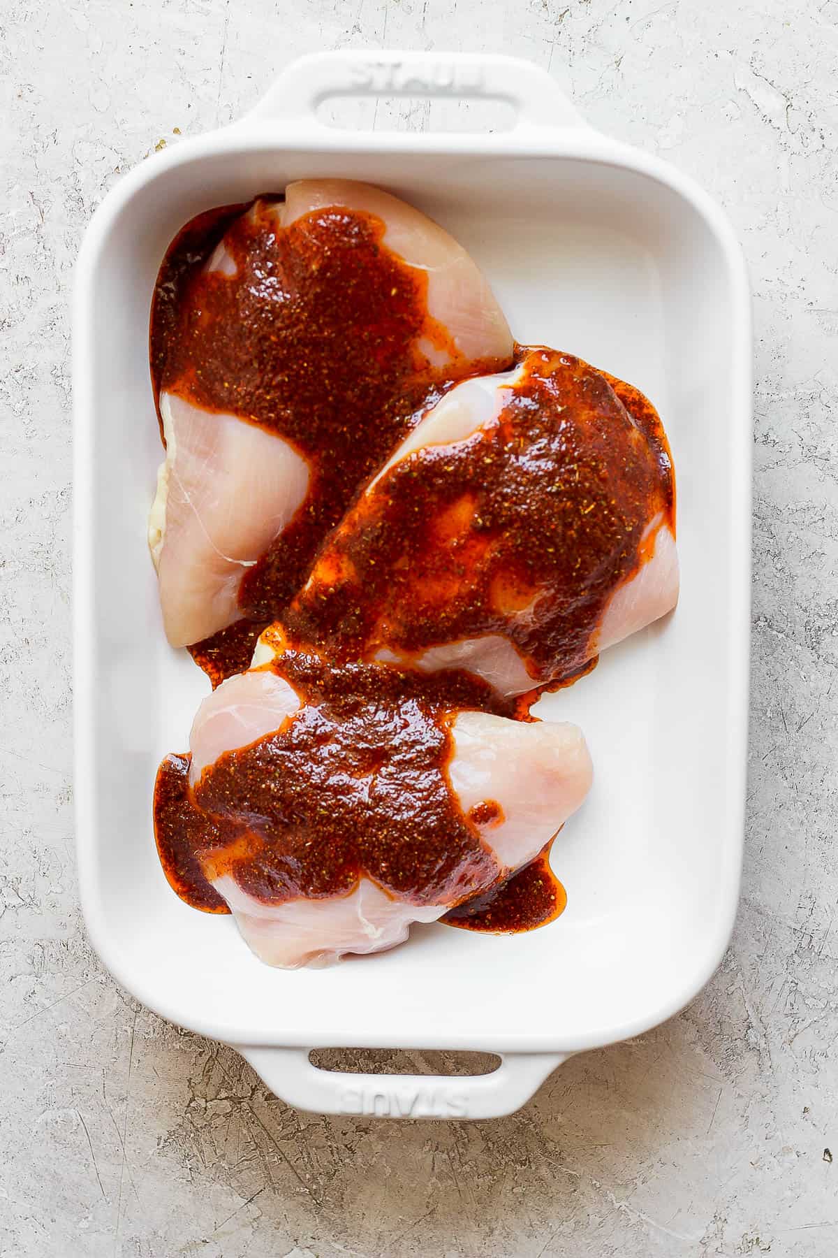 The marinade poured over whole chicken breasts in a white baking dish.