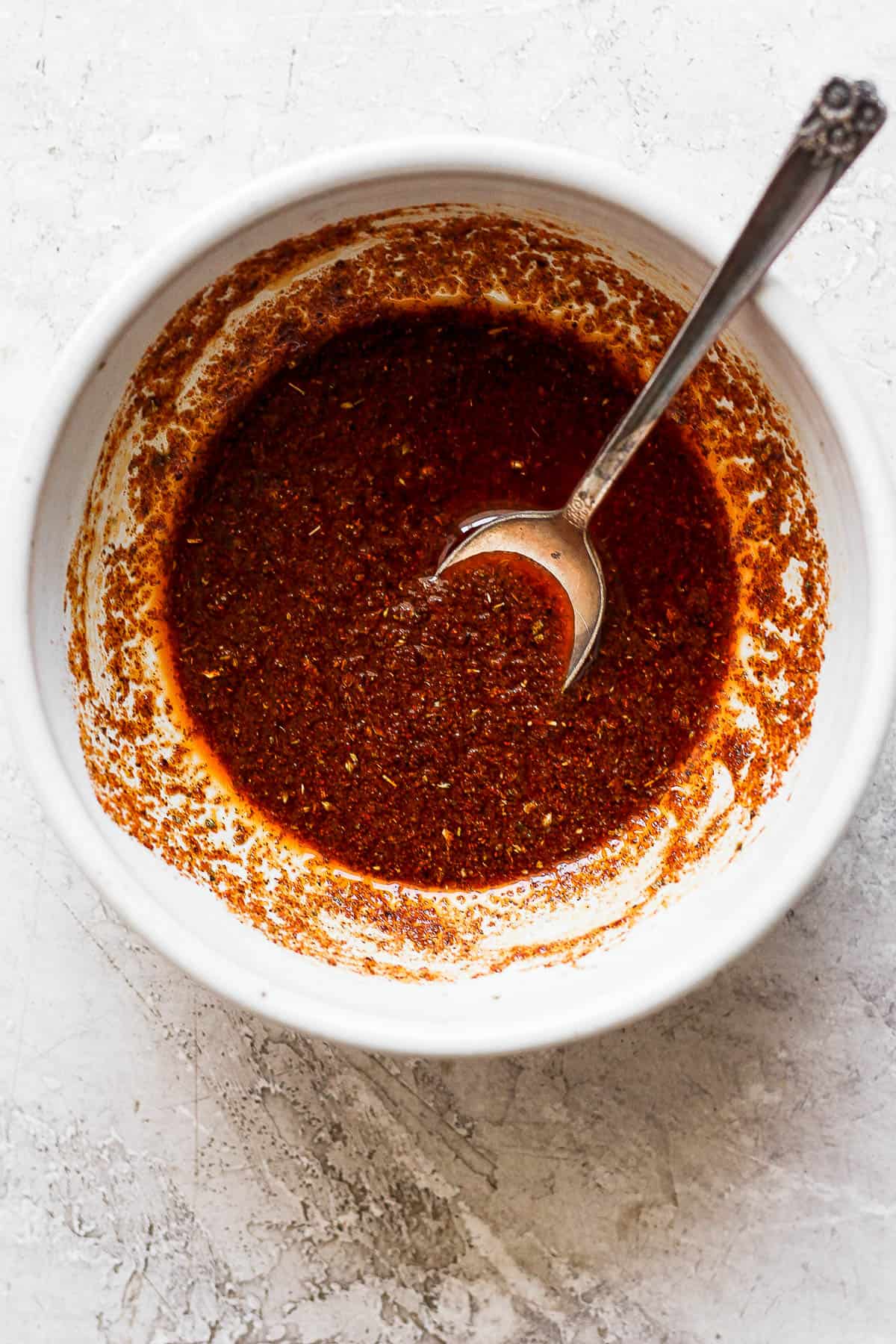 The chicken fajita marinade all mixed together in a bowl with a spoon.