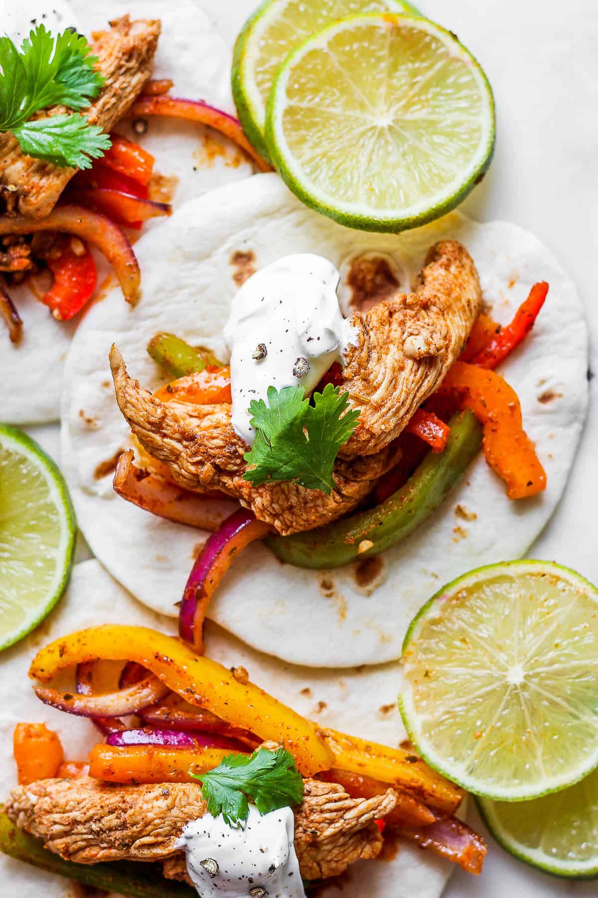 Chicken fajita mixture in a tortilla with sour cream and cilantro on top.