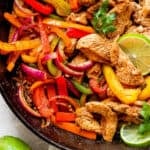 Top down shot of a cast iron skillet filled with chicken fajitas with lime slices and cilantro.