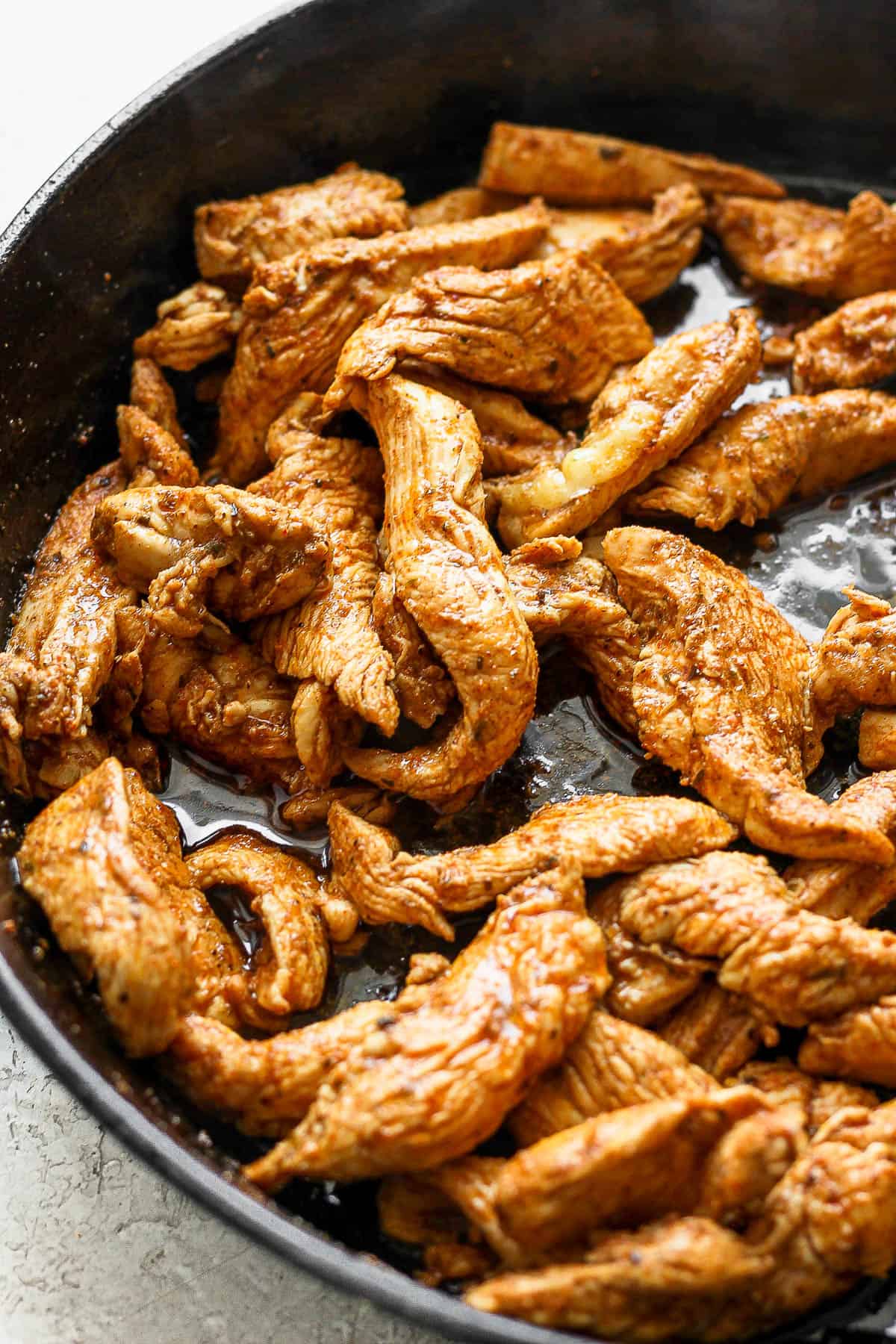 Marinated chicken tenders searing in a cast iron skillet.