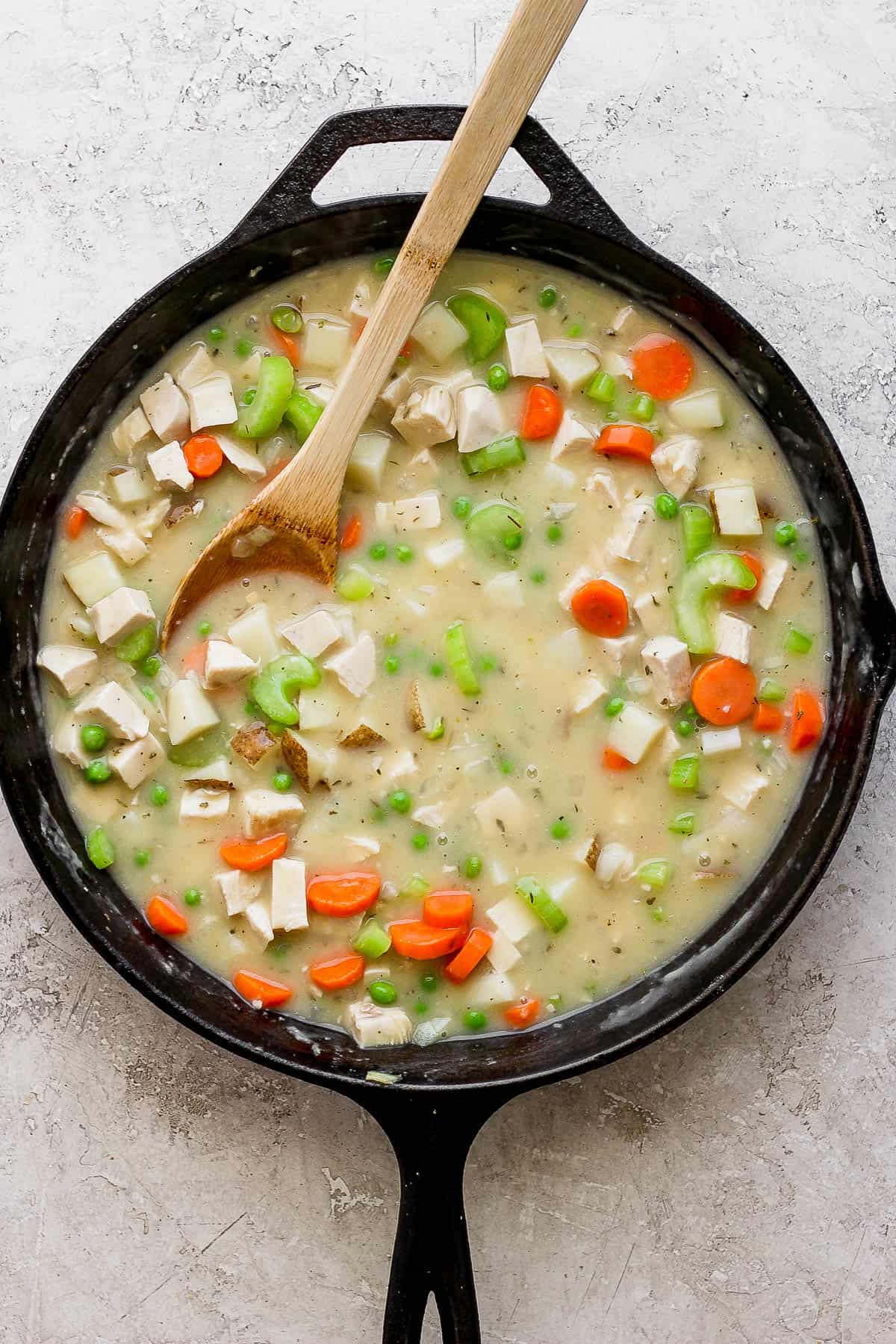 The entire chicken pot pie filling mixed together in the cast iron skillet with a wooden spoon.