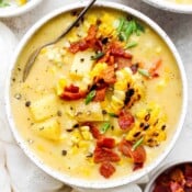 Top down shot of a bowl of corn chowder with bacon bits and chopped chive on top.