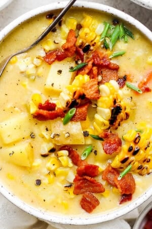 Top down shot of a bowl of corn chowder with bacon bits and chopped chive on top.