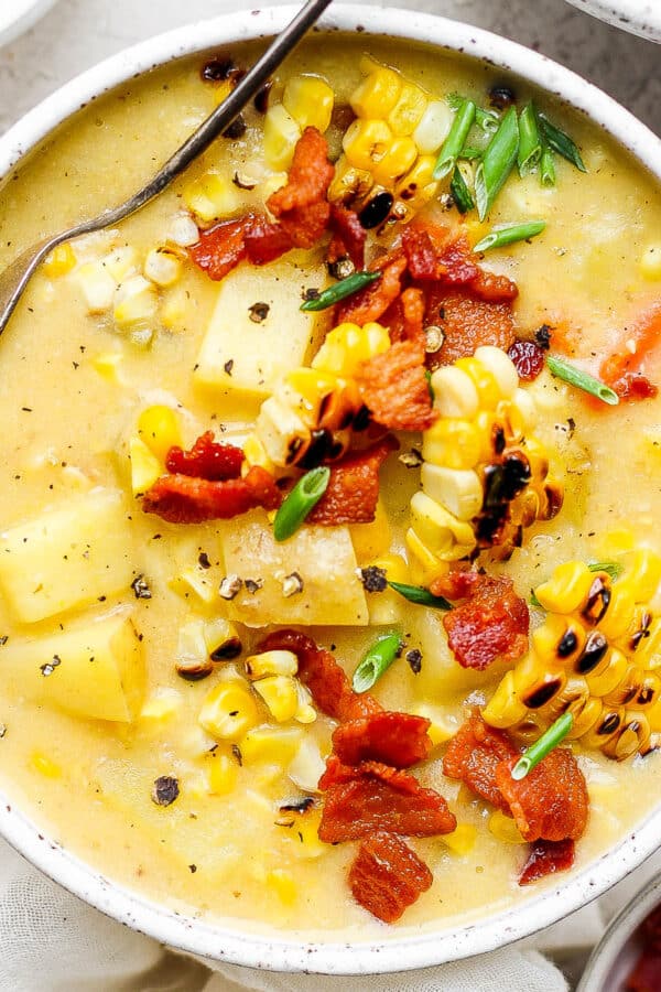 Top down shot of a bowl of corn chowder with bacon bits and chopped chive on top.