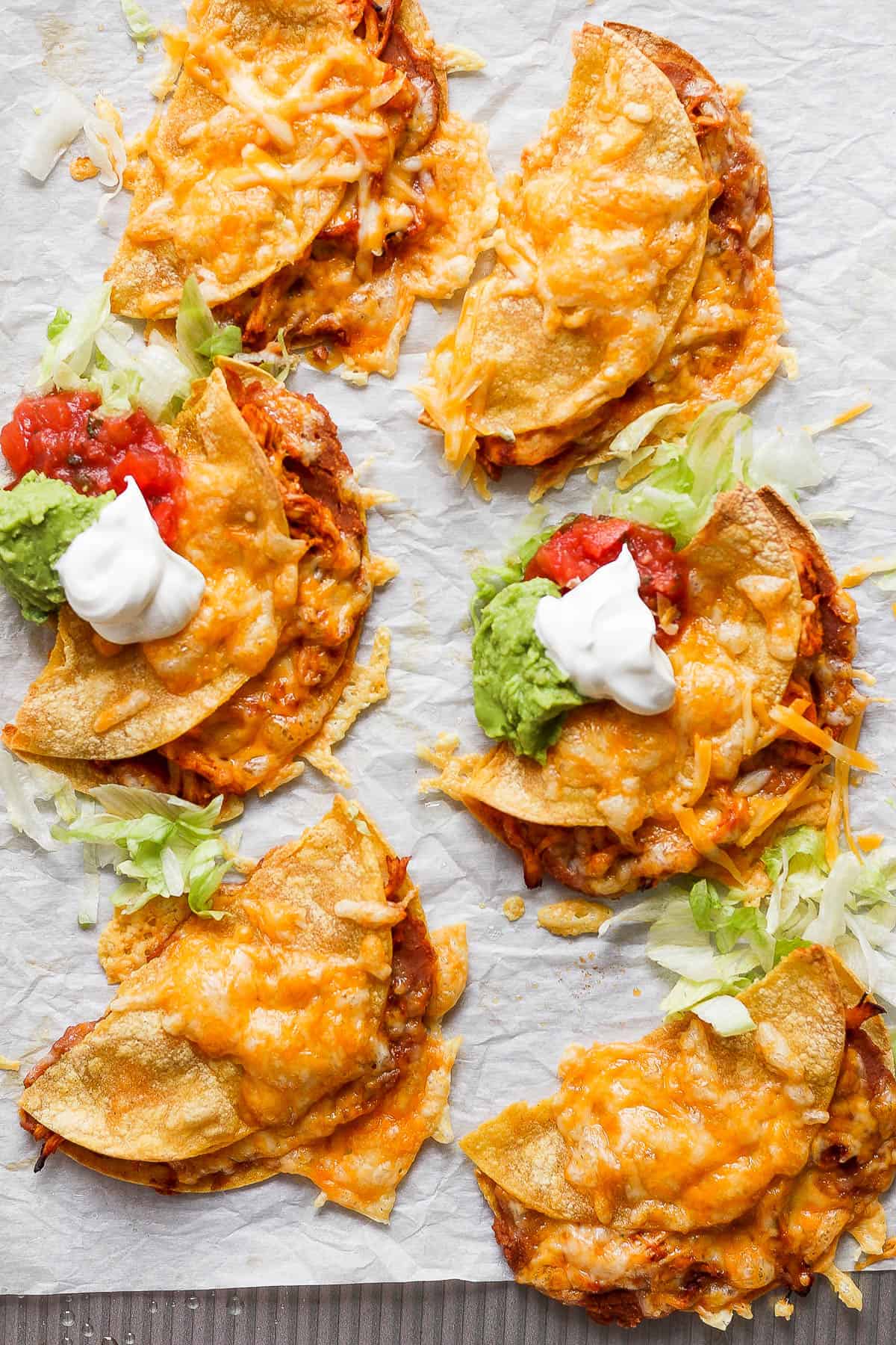 Crispy chicken tacos on parchment paper after baking.