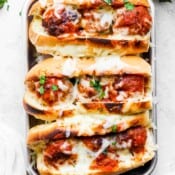 Top down shot of a small tray of three meatball subs with melted cheese on top.