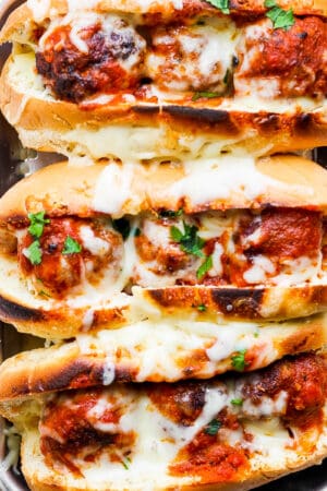 Top down shot of a small tray of three meatball subs with melted cheese on top.