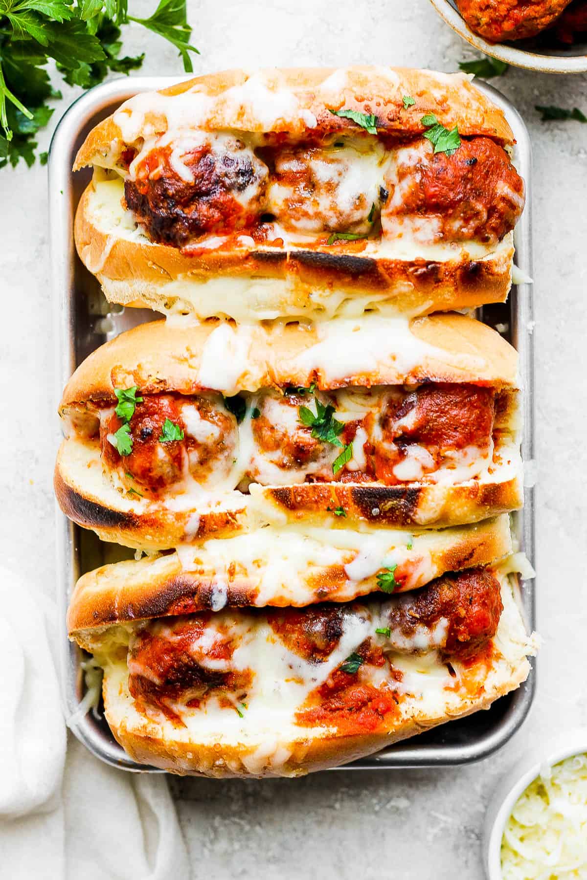 Three broiled meatball subs sprinkled with fresh parsley.