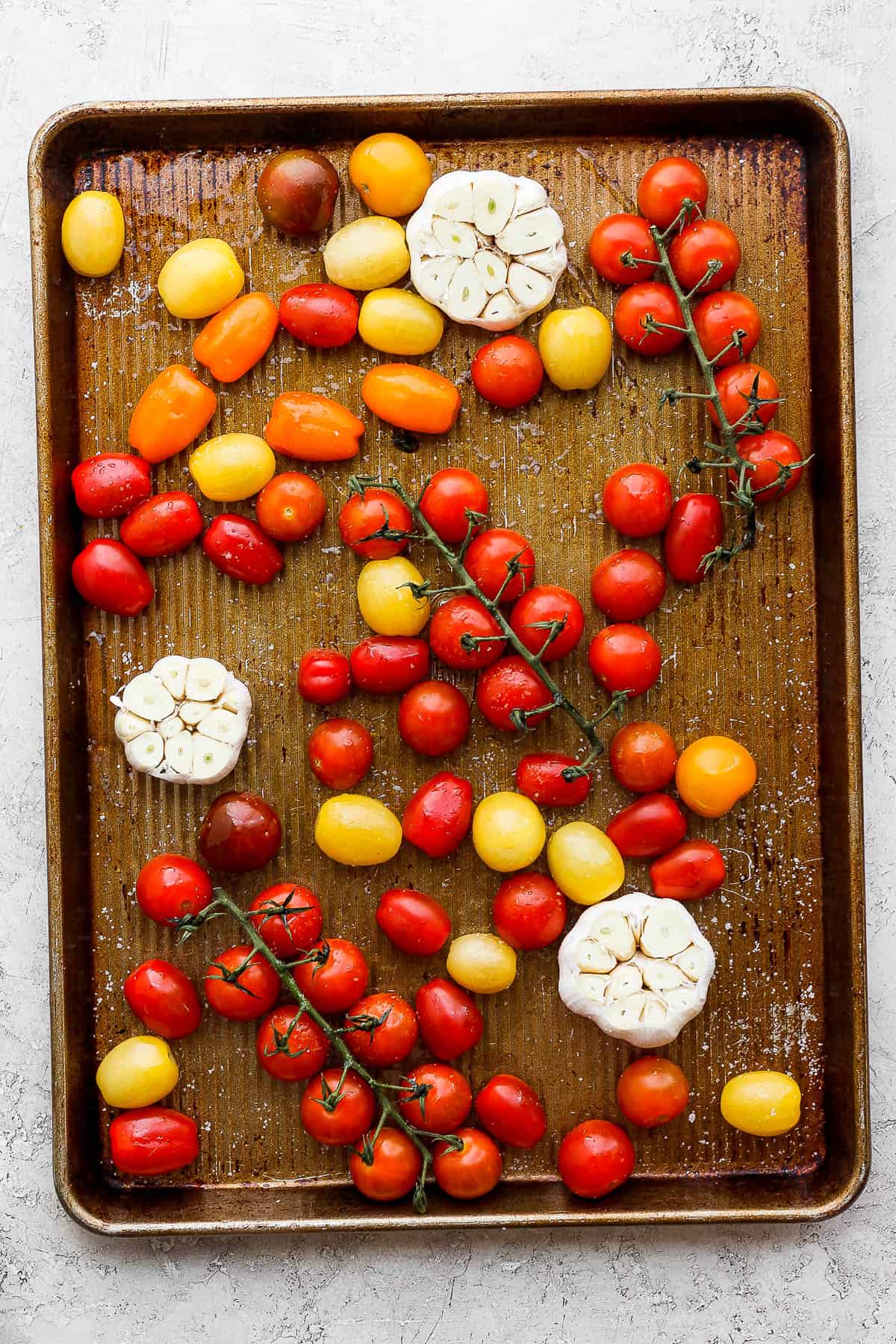 Cherry tomatoes on a baking sheet drizzled with olive oil and sprinkled with salt and pepper.