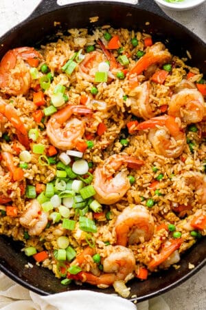 Top down shot of a cast iron skillet filled with shrimp fried rice with green onions on top and a little bowl of sauce next to it.