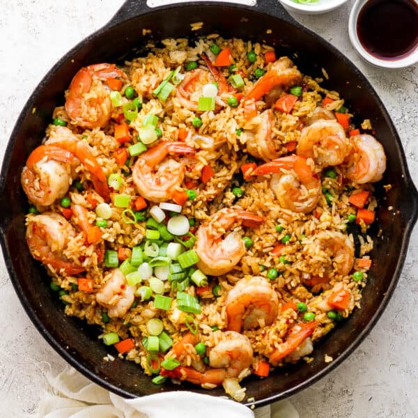 Top down shot of a cast iron skillet filled with shrimp fried rice with green onions on top and a little bowl of sauce next to it.