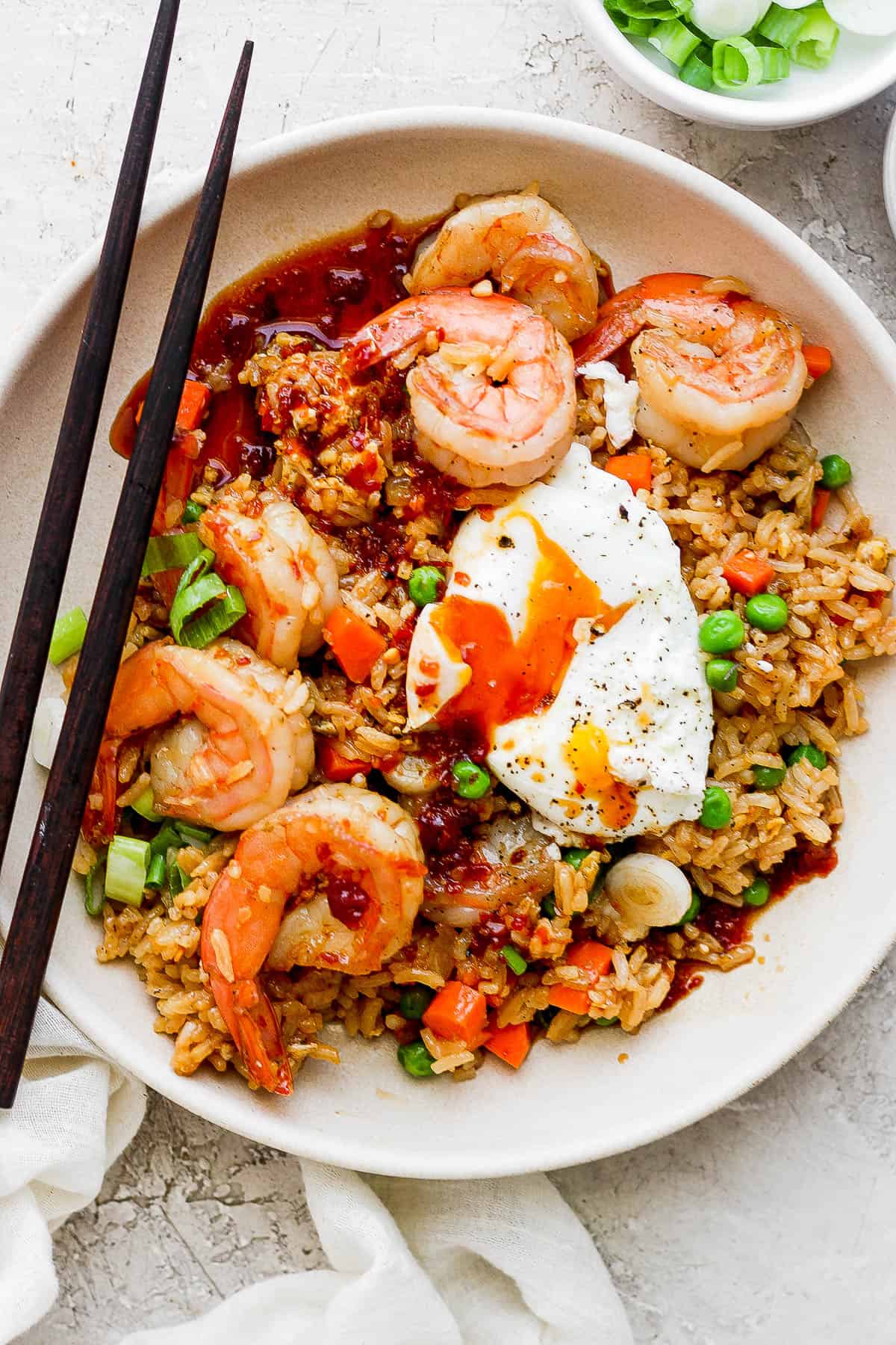 Shrimp fried rice in a bowl with chop sticks off to the side and a soft boiled egg on top.