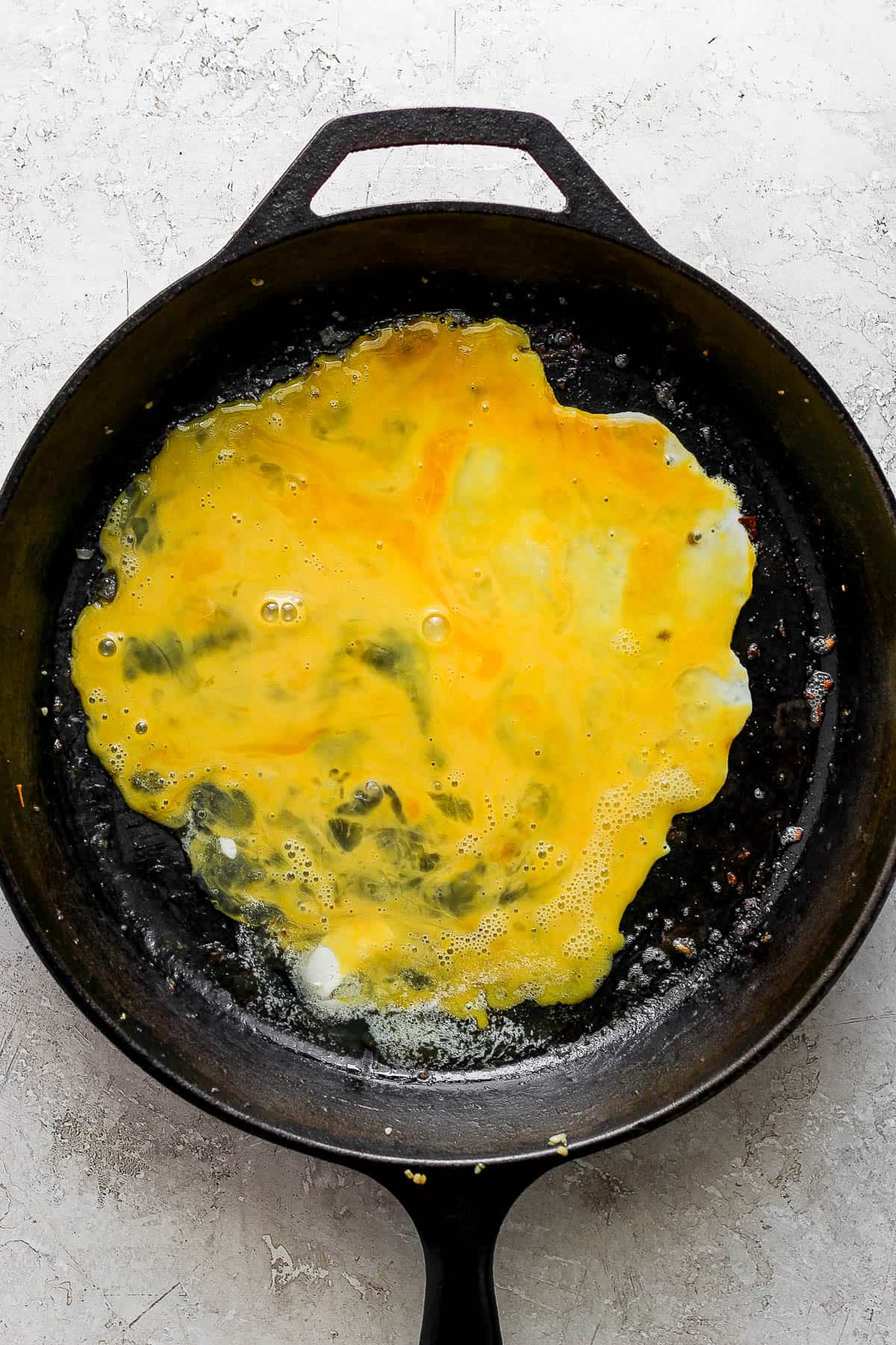 An uncooked whisked egg in the bottom of the skillet.