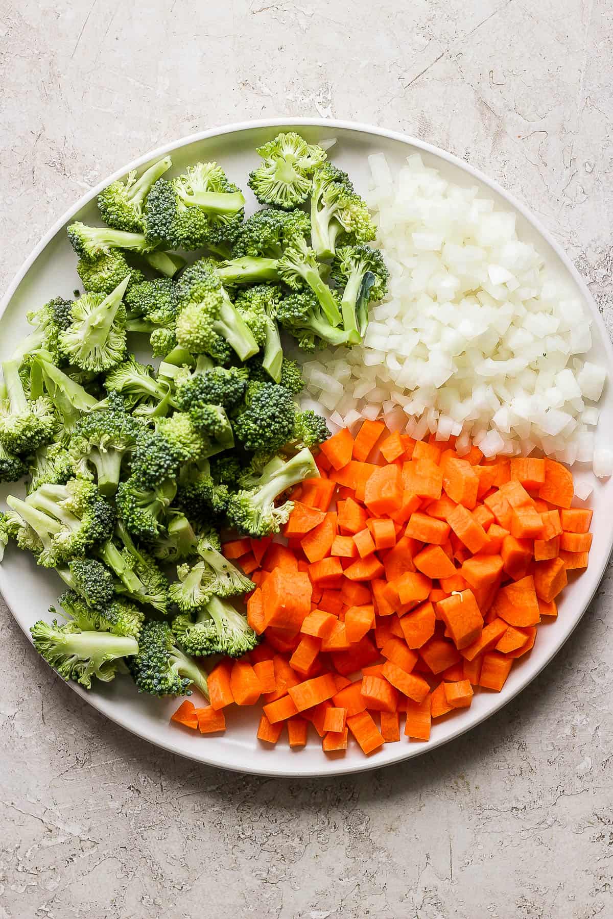 Chopped onion, carrots, and broccoli florets on a white plate.