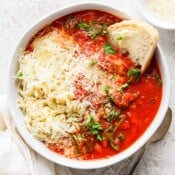 Top down shot of a bowl of tomato florentine soup with orzo, parmesan cheese and piece of sourdough bread sticking out.