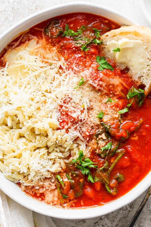 Top down shot of a bowl of tomato florentine soup with orzo, parmesan cheese and piece of sourdough bread sticking out.