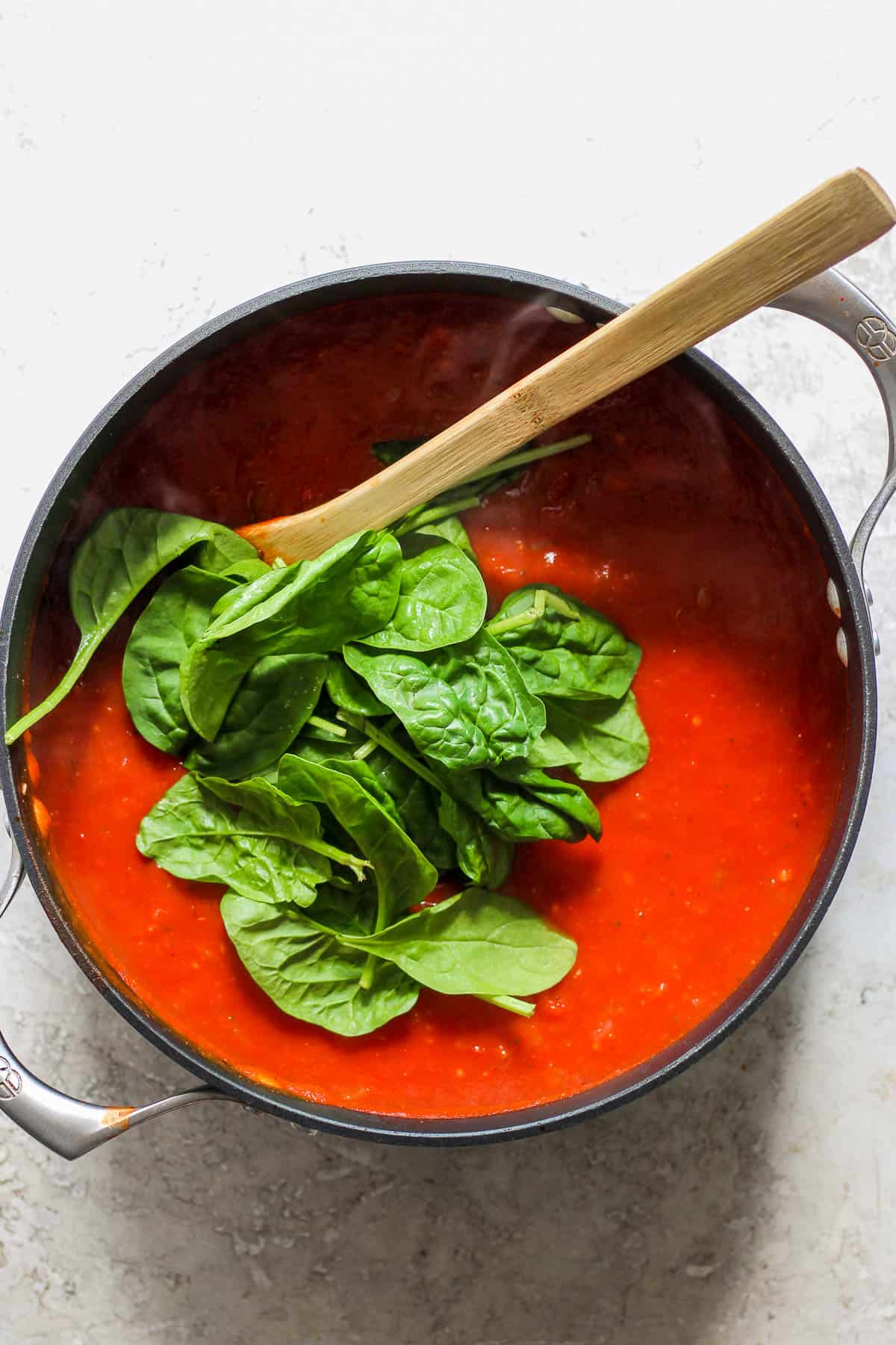 Spinach leaves toss in to the pot of soup and a wooden spoon.