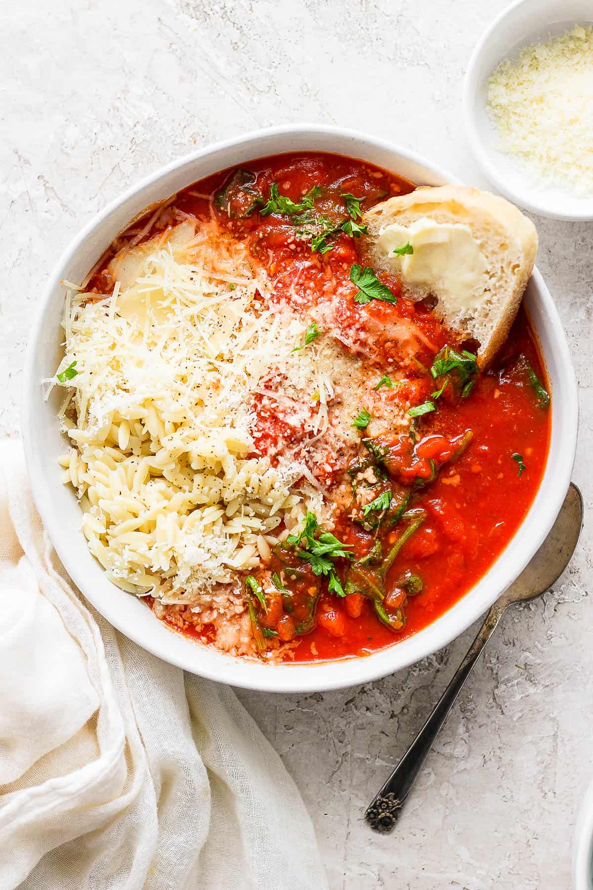 A fully topped bowl of tomato florentine soup with a small bowl of parmesan cheese on the side.