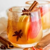 A glass filled with an apple cider margarita with apple slices inside, star anise and a cinnamon stick.