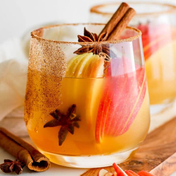 A glass filled with an apple cider margarita with apple slices inside, star anise and a cinnamon stick.